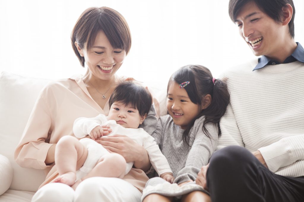 Parents, daughter and baby are sitting on the sofa and talking.