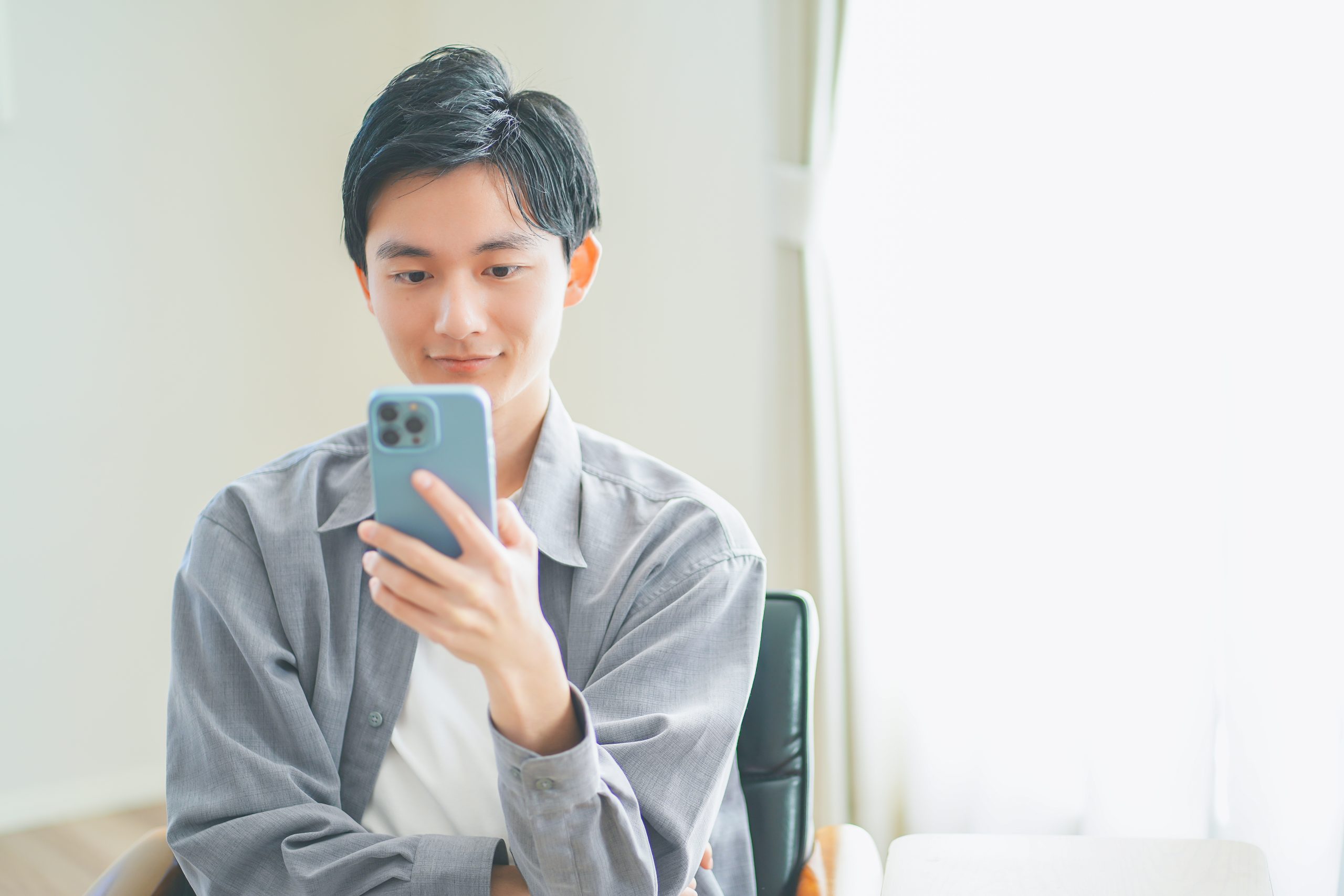 ソファに座ってスマートフォンを操作する若い