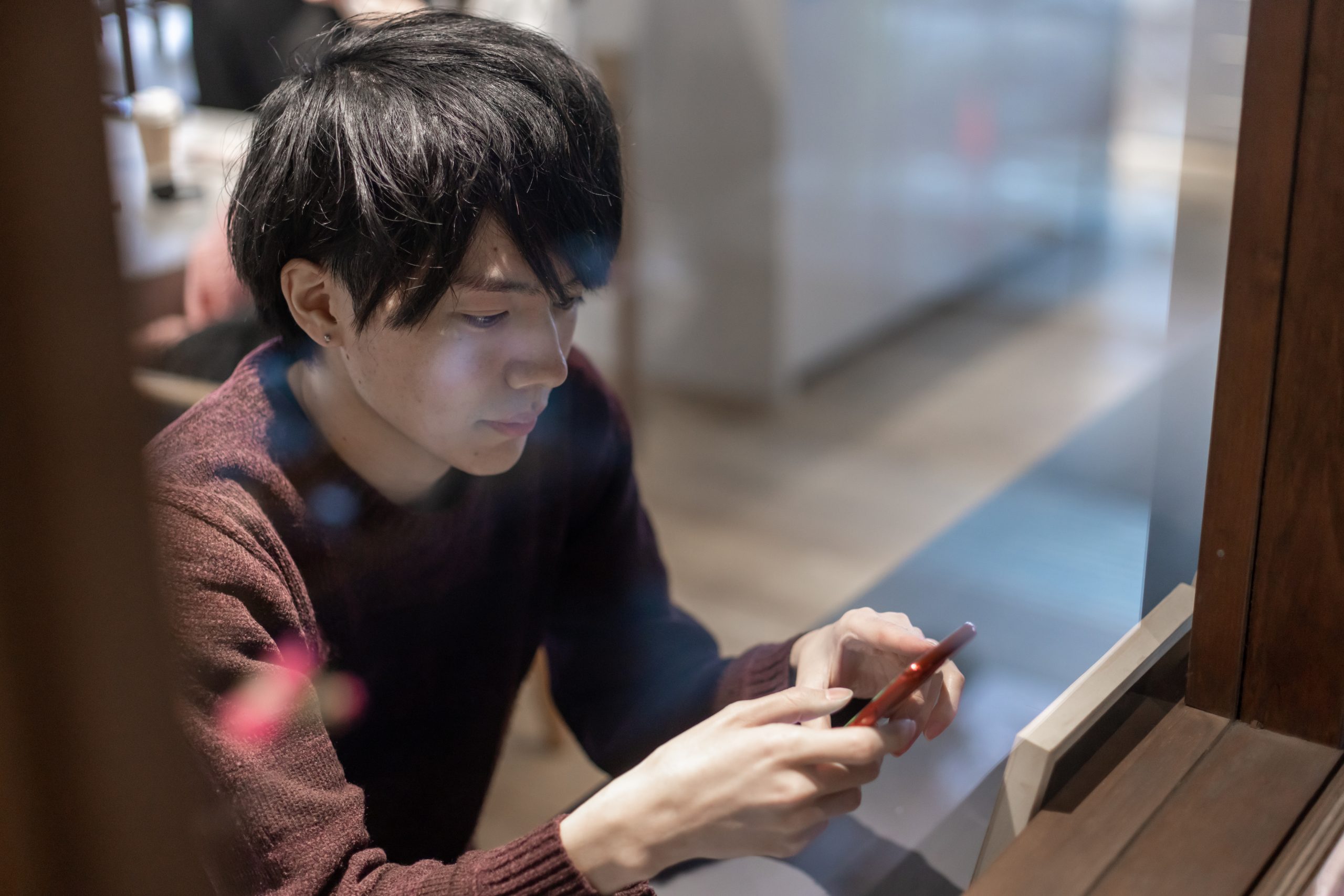 カフェの窓辺でスマートフォンを操作する20代男性